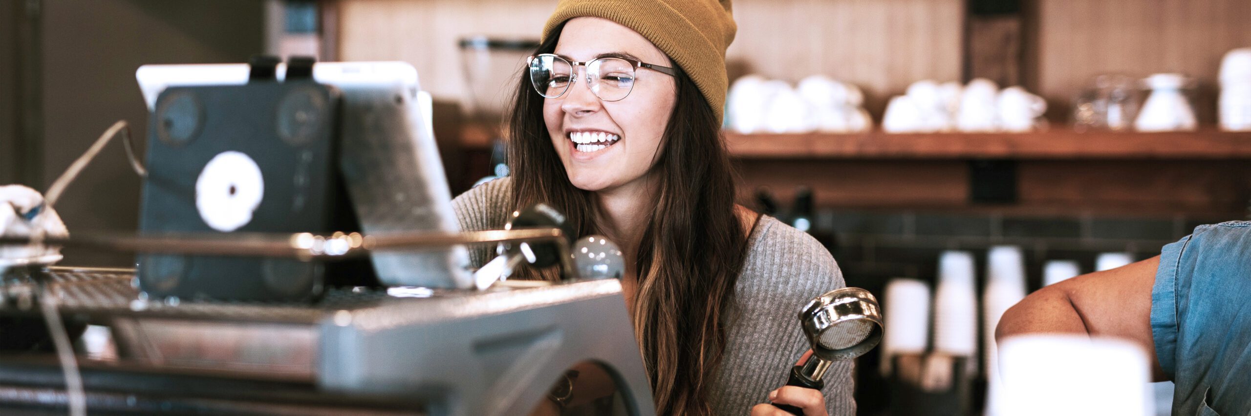 female smiling behind espresso machine, holding onto a portafilter