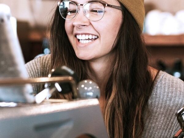 female smiling behind espresso machine, holding onto a portafilter