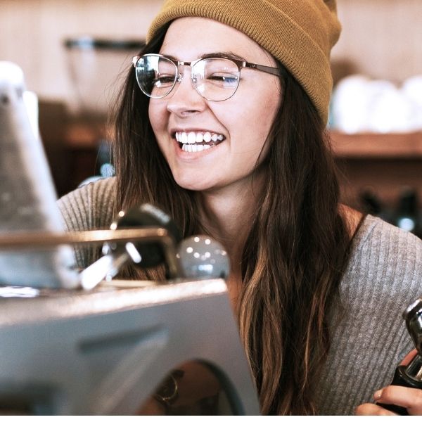 female smiling behind espresso machine, holding onto a portafilter