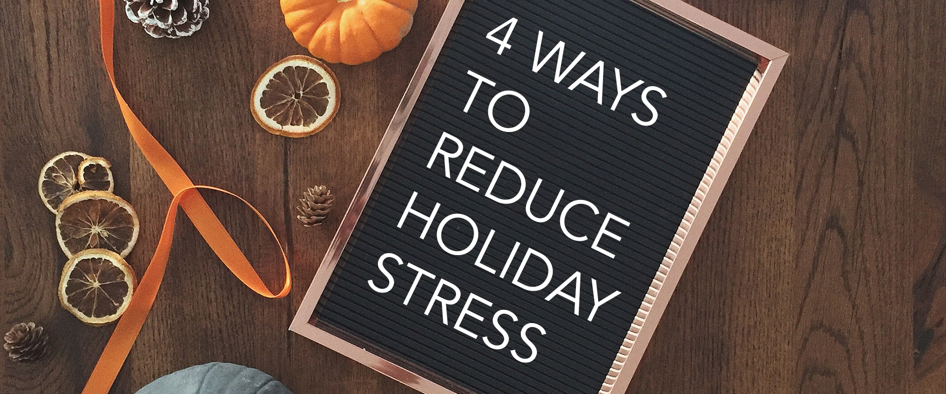 Felt letter board titled "4 Ways to Reduce Holiday Stress" next to dried orange slices, a orange ribbon, a pumpkin, and pinecones