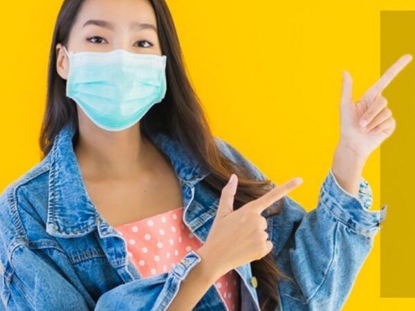 Young Asian woman with a face mask on pointing to the right