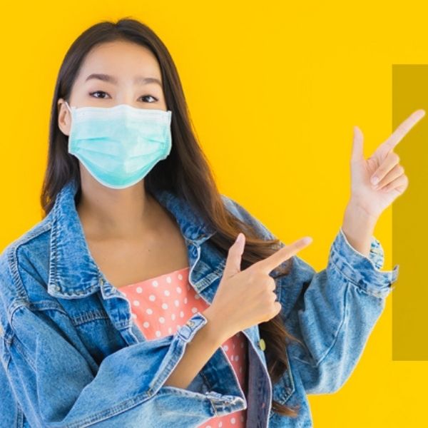 Young Asian woman with a face mask on pointing to the right