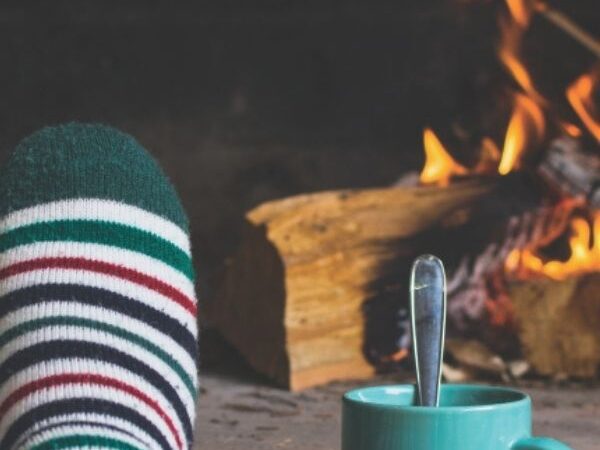 foot with a stripped sock next to a blue mug in front of a lit fireplace