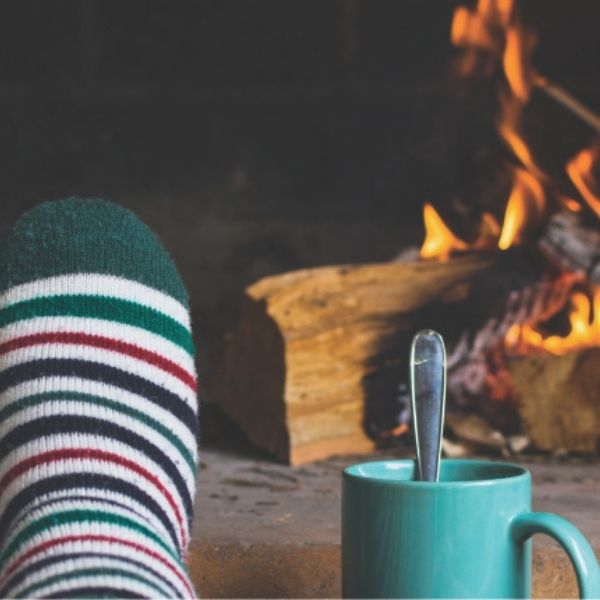 foot with a stripped sock next to a blue mug in front of a lit fireplace