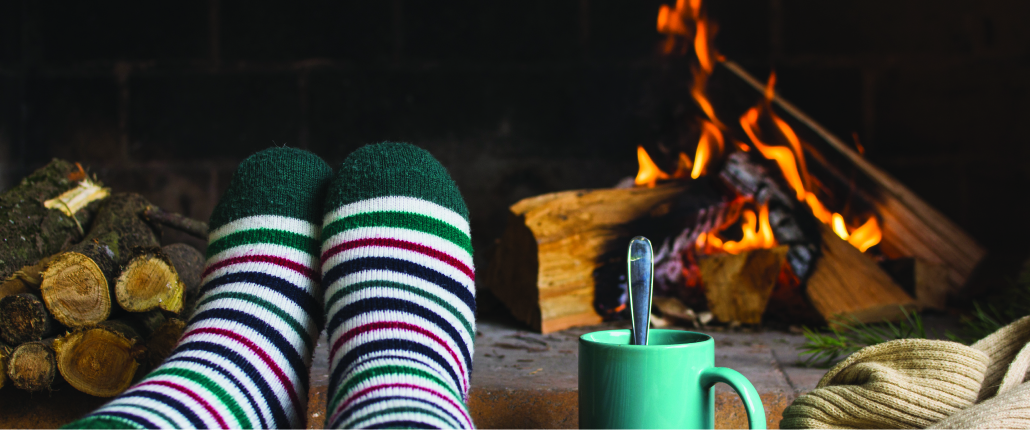 December 2020 Blog header image of foot with a stripped sock next to a blue mug in front of a lit fireplace