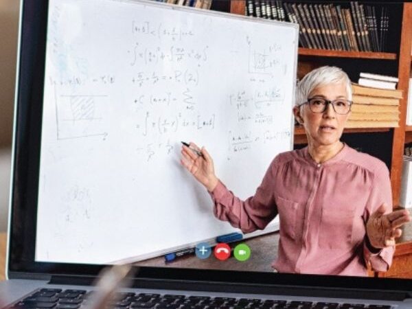 closeup of a laptop, teacher on the screen in front of a white board with math on the board