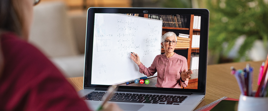 over the shoulder photo of a student looking at her laptop, doing an online math class with her teacher on the screen