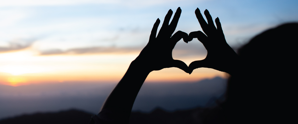 two hands making a heart shape with a sunset in the background