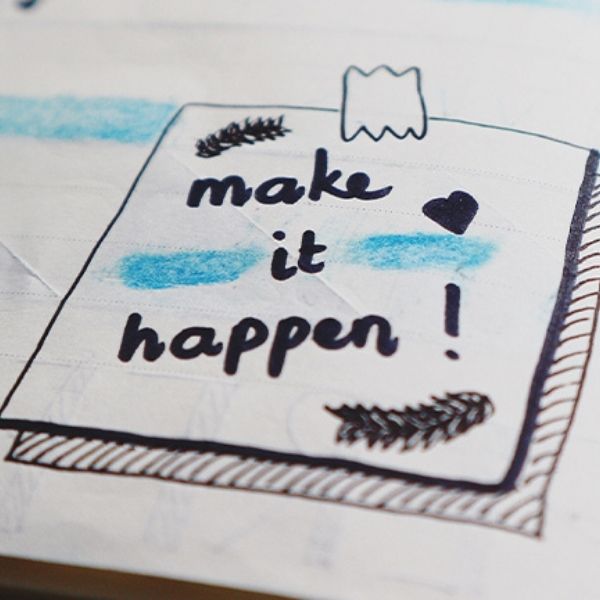 planner open to a doddle of drawing that says "Make it Happen!" with blue highlights