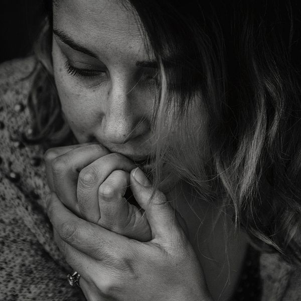 a close up of a black and white image of a pensive young woman with her hands to her face