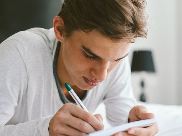 a teenaged male laying on a bed, journaling