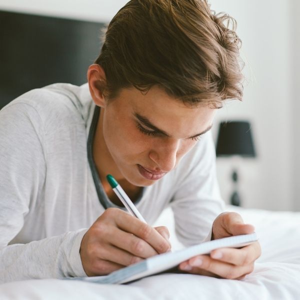 a teenaged male laying on a bed, journaling