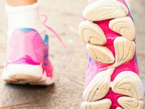 close up of two feet walking on cement wearing hot pink and white athletic shoes