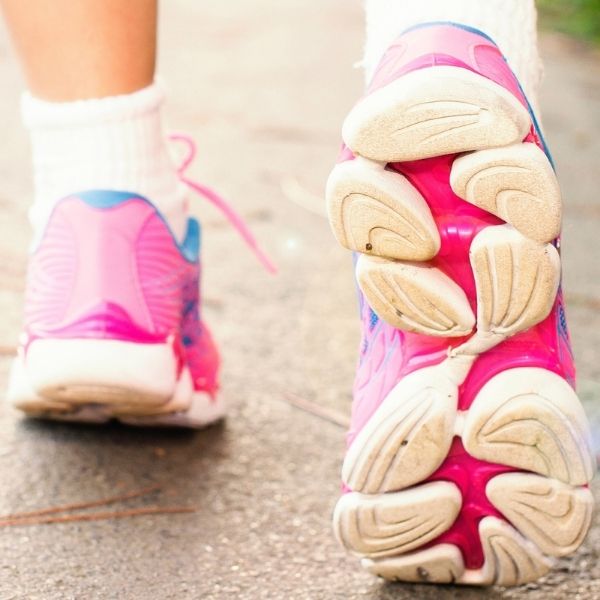 close up of two feet walking on cement wearing hot pink and white athletic shoes