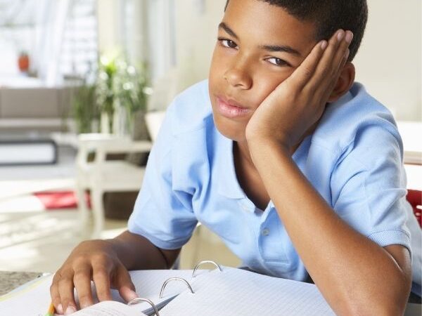 young boy leaning on his hand, frustrated, with homework beneath him