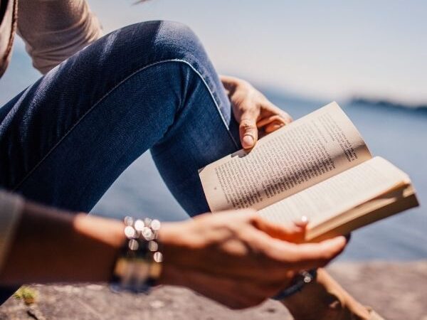 a closeup of a person reading near a body of water with the title overlay "How to Prepare In the Summer Before College"