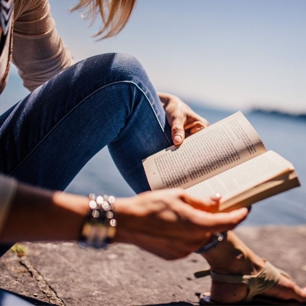 a closeup of a person reading near a body of water with the title overlay "How to Prepare In the Summer Before College"