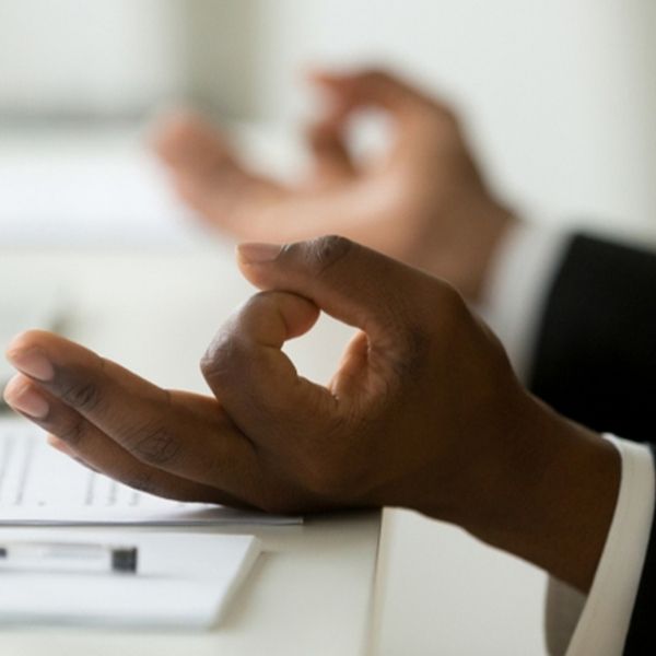 closeup of a black person wearing a formal work suit, meditating at their work desk