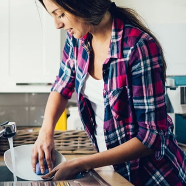 Young woman leaning over the counter, washing a dish with the water running