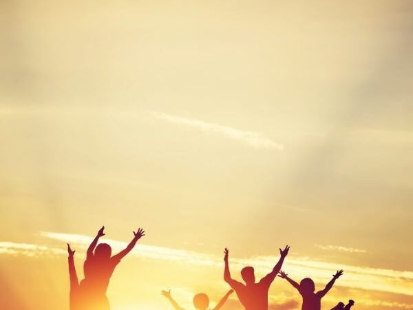 Group of silhouetted people with arms stretched out to the sky at sunset