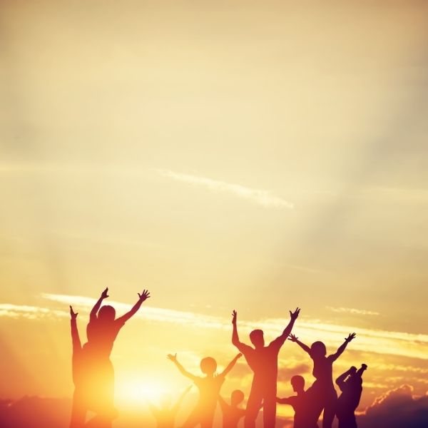 Group of silhouetted people with arms stretched out to the sky at sunset