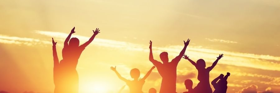 Group of silhouetted people with arms stretched out to the sky at sunset