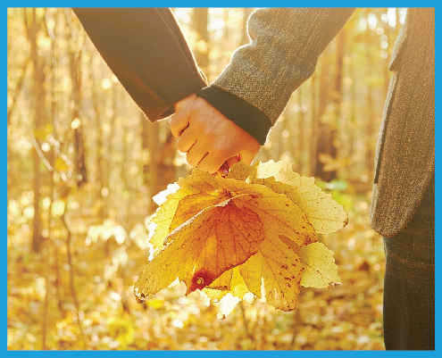 two hands holding each other, with a bouquet of autumn leaves