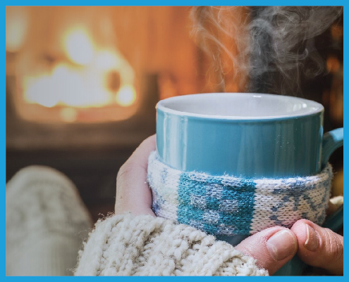 Dec blog feature image of two hands holding a mug with steam, in front of a lit fireplace